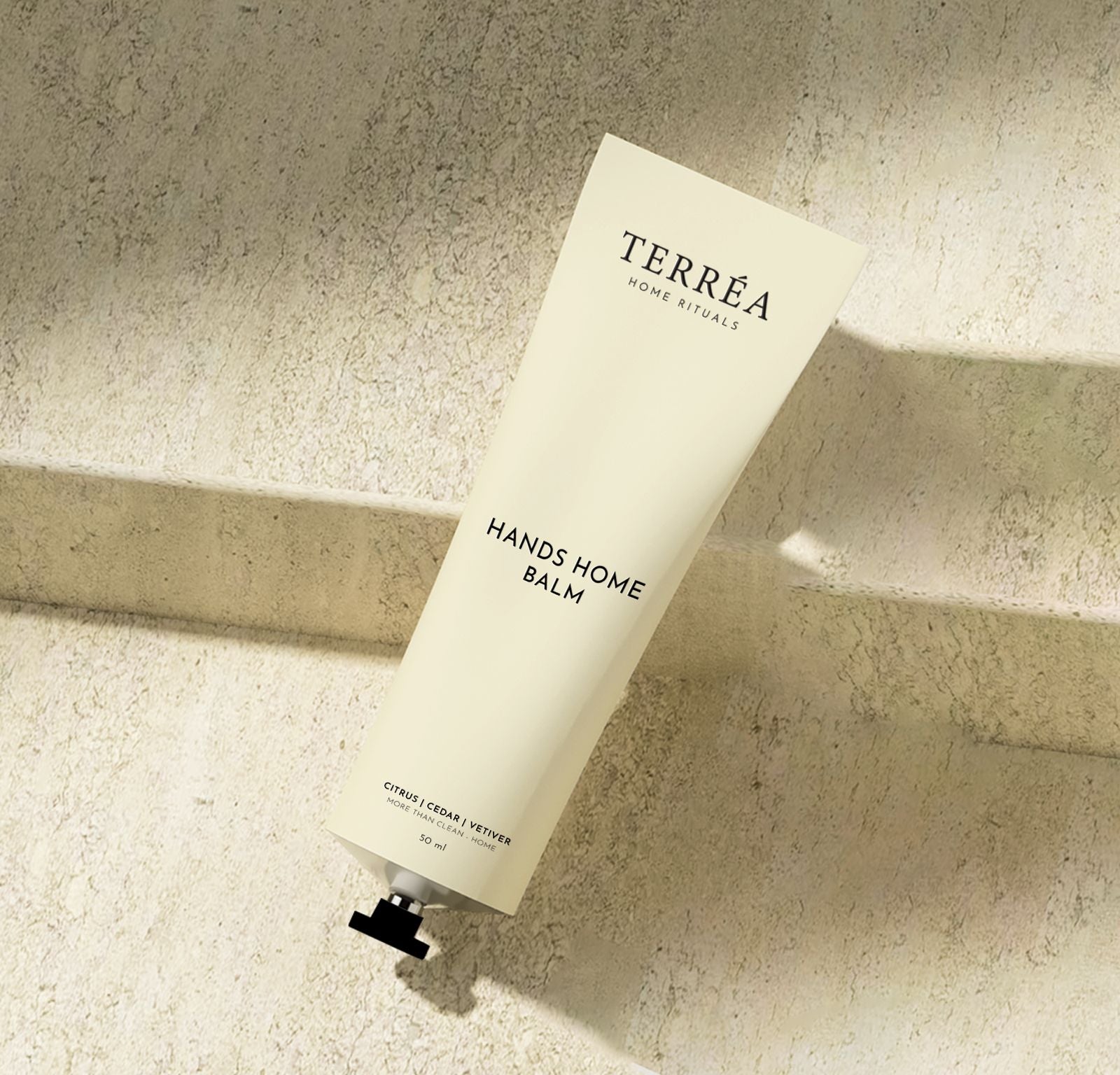 Terréa Hands Home Balm tube on a textured stone surface with soft natural shadows.