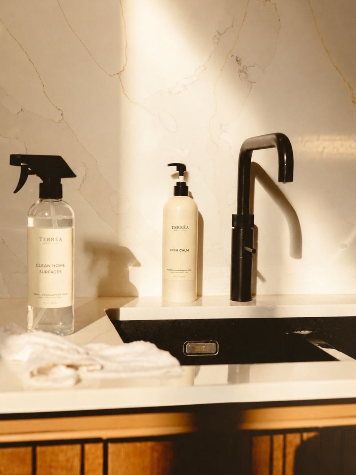 Terréa Clean Home Surfaces and Dish Calm bottles styled beside a black sink and tap in warm afternoon light.