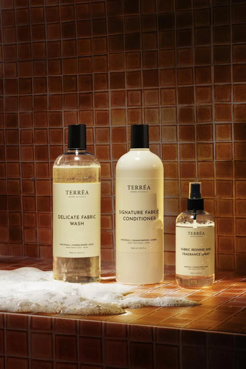 Three bottles of Terrea fabric care products on a tiled surface with a brown tile background.