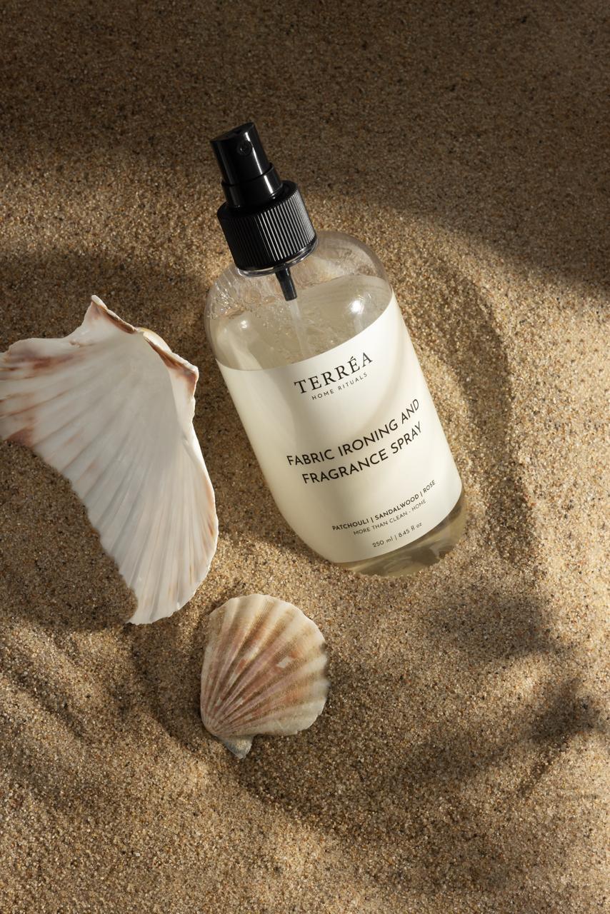 Fabric ironing and fragrance spray with seashells on sandy beach, eco-friendly home care