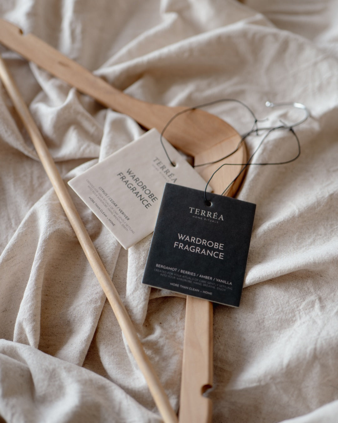 Terréa Wardrobe Fragrance tags resting on soft linen with wooden hangers, creating a quiet wardrobe-care ritual.