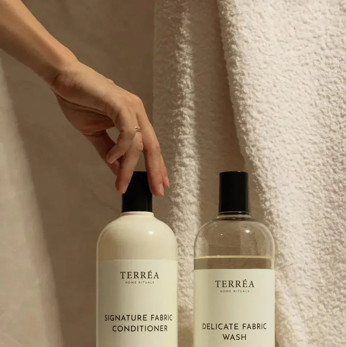 Hand reaching for TERRÉA Signature Fabric Conditioner and Delicate Fabric Wash bottles beside soft towel
