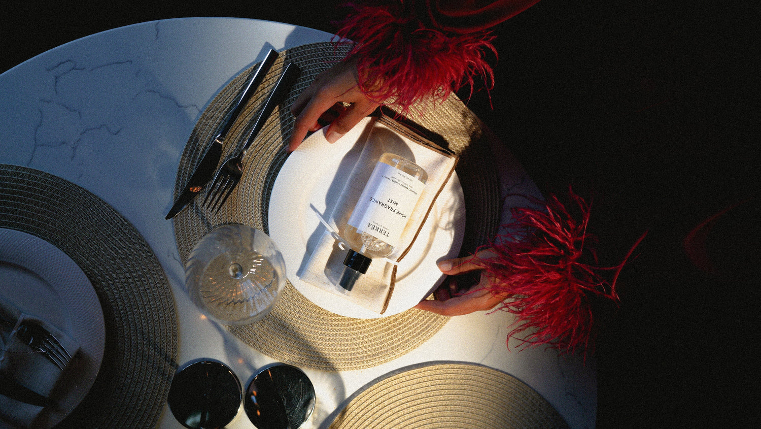 Elegant home fragrance mist on a luxury dining table with red feather accents and woven placemats.