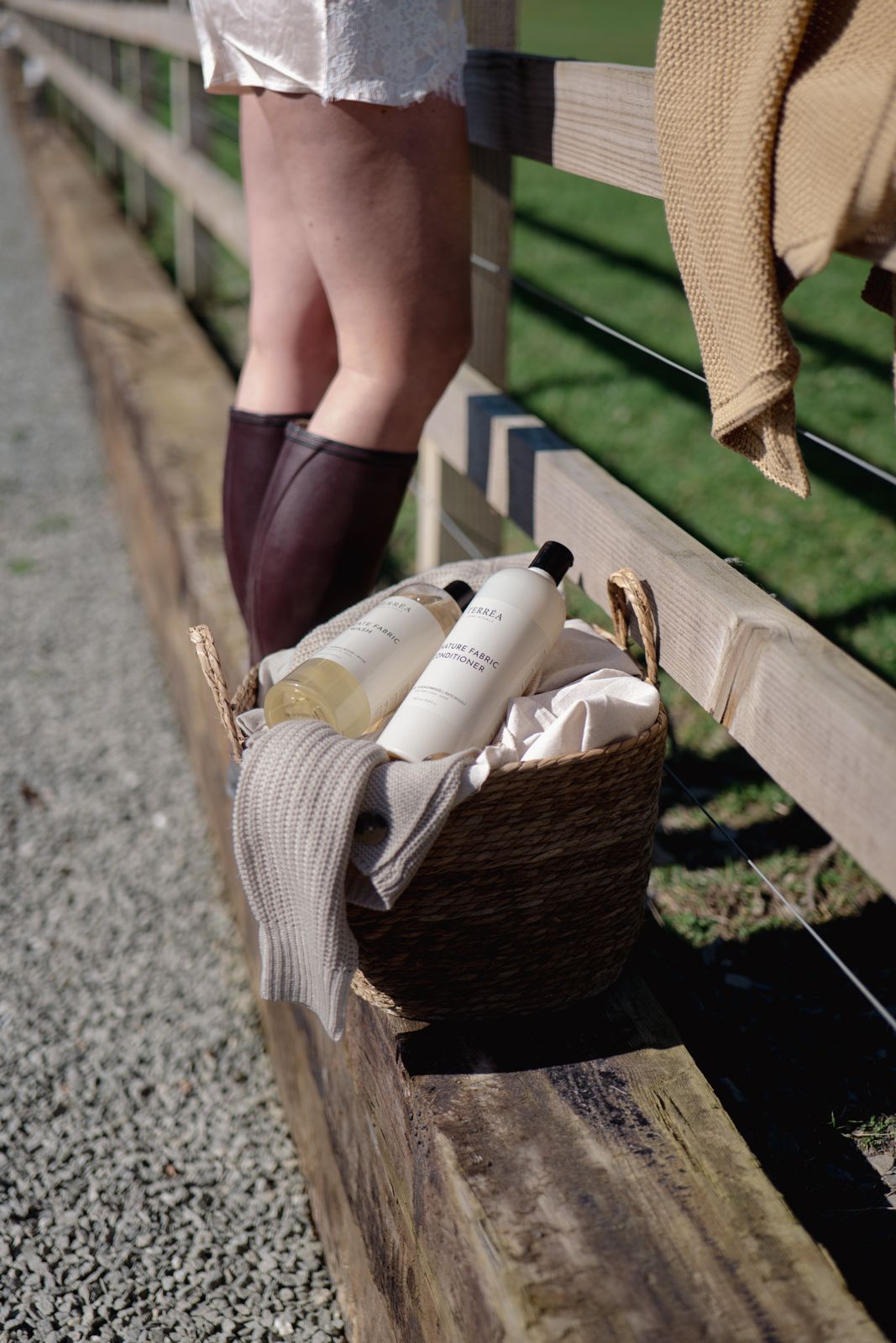 Eco-friendly fabric care products in woven basket beside person in boots, rustic outdoor setting