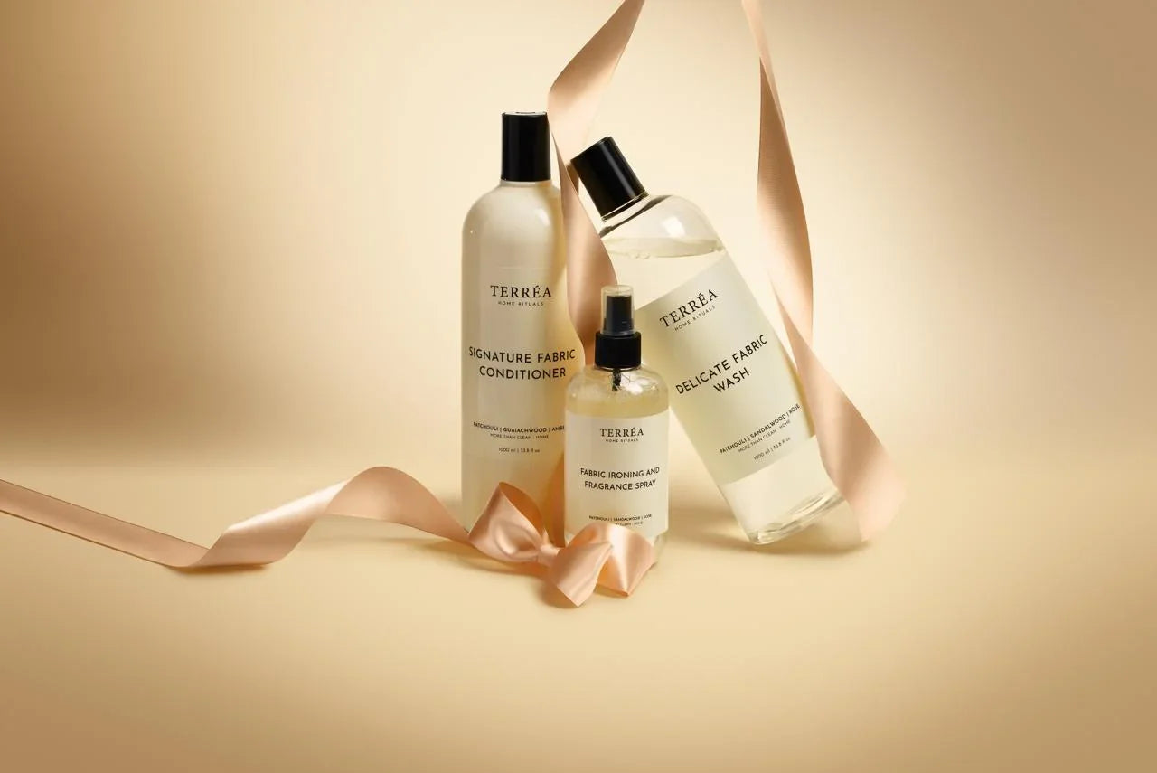 Terréa Signature Fabric Conditioner and Delicate Fabric Wash with a small fabric spray, styled on a warm beige background with a champagne satin ribbon.