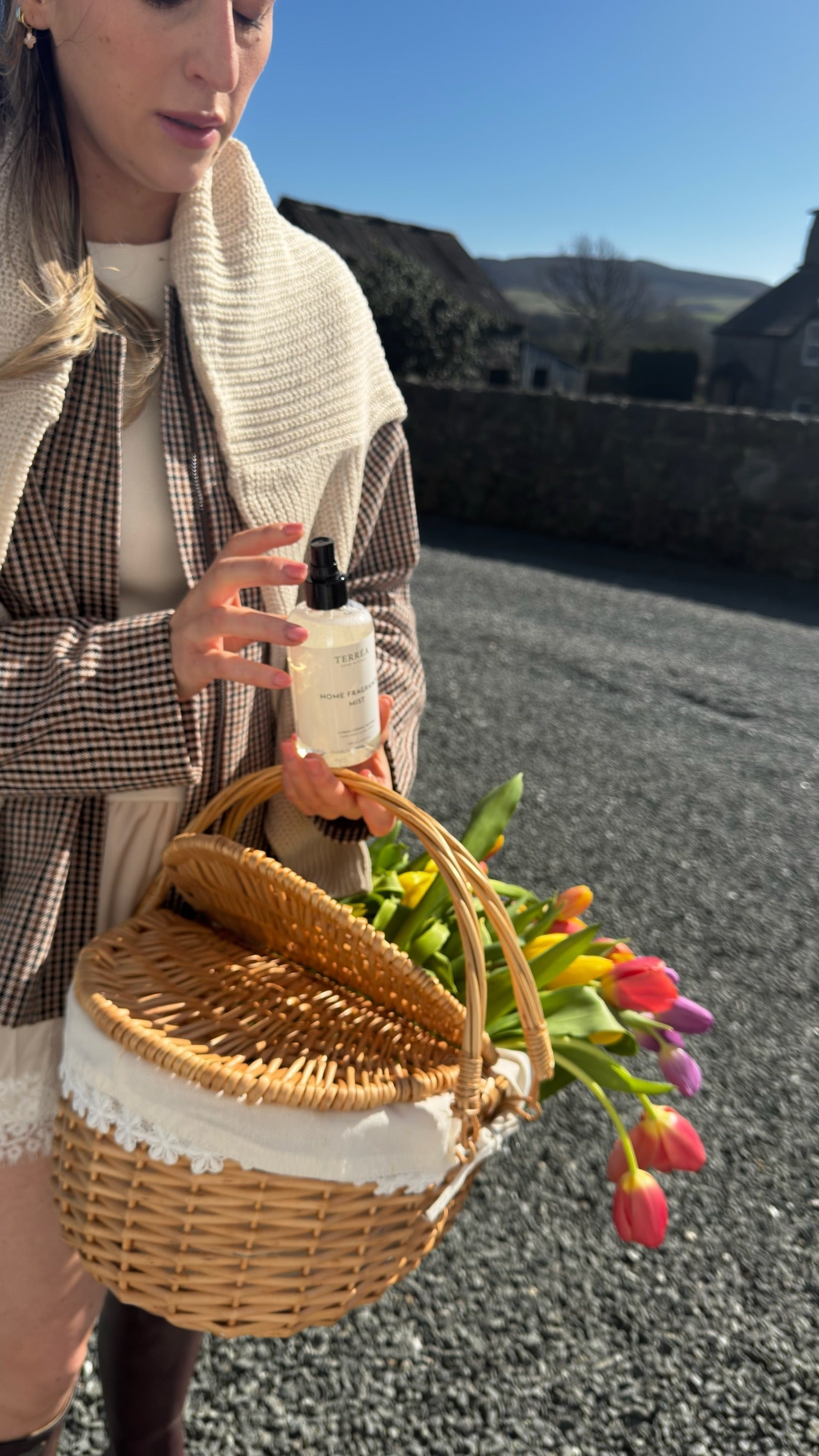 Woman holding home fragrance mist and wicker basket with tulips, eco-conscious home care