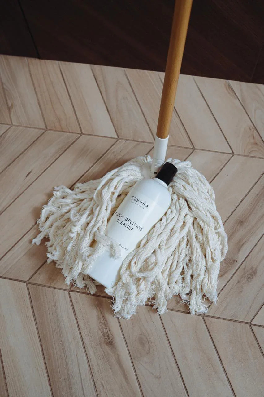 Eco-friendly floor delicate cleaner bottle resting on cotton mop head on wooden tile floor