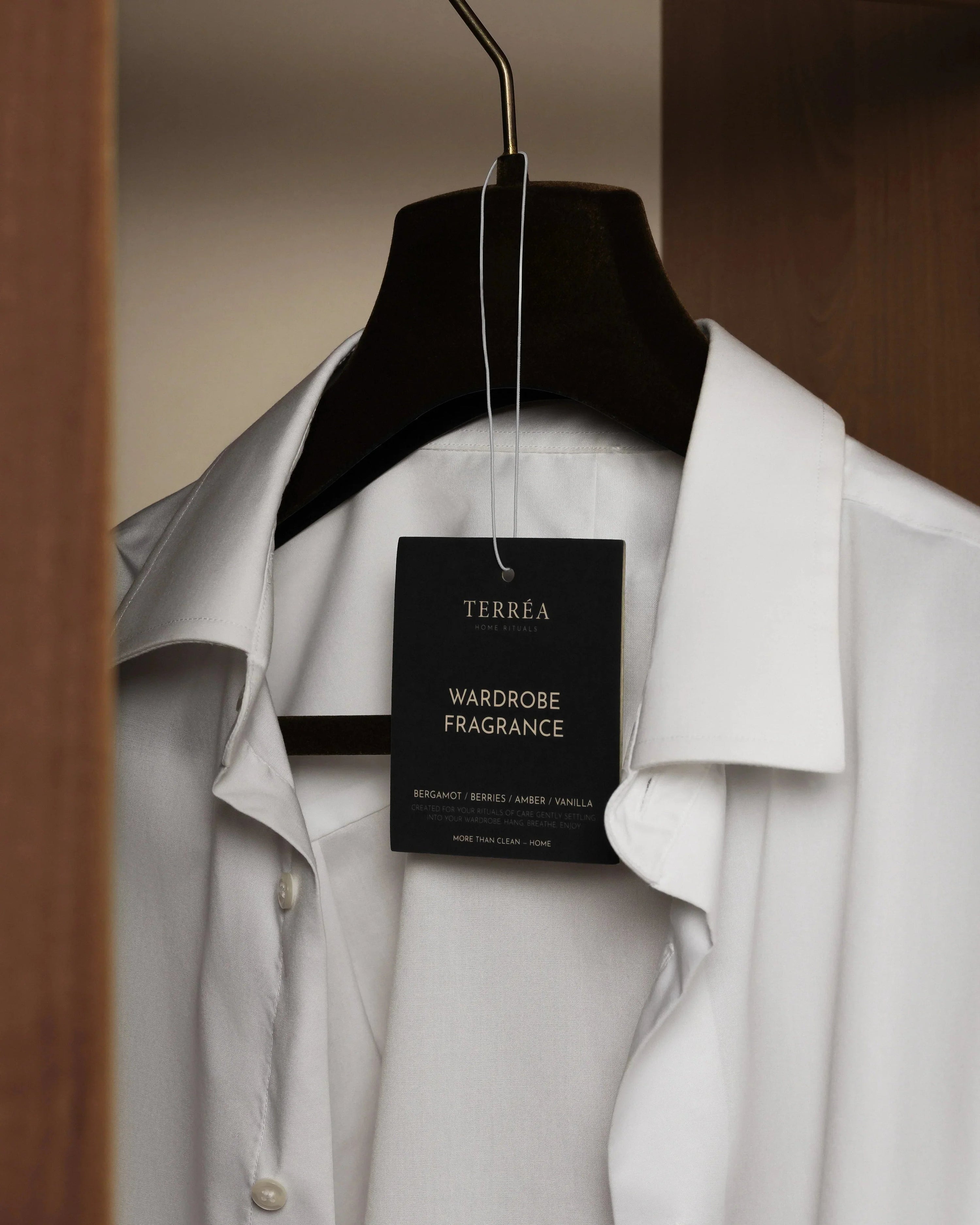 Wardrobe fragrance tag on white shirt, featuring bergamot, berries, amber, vanilla scents for home rituals.
