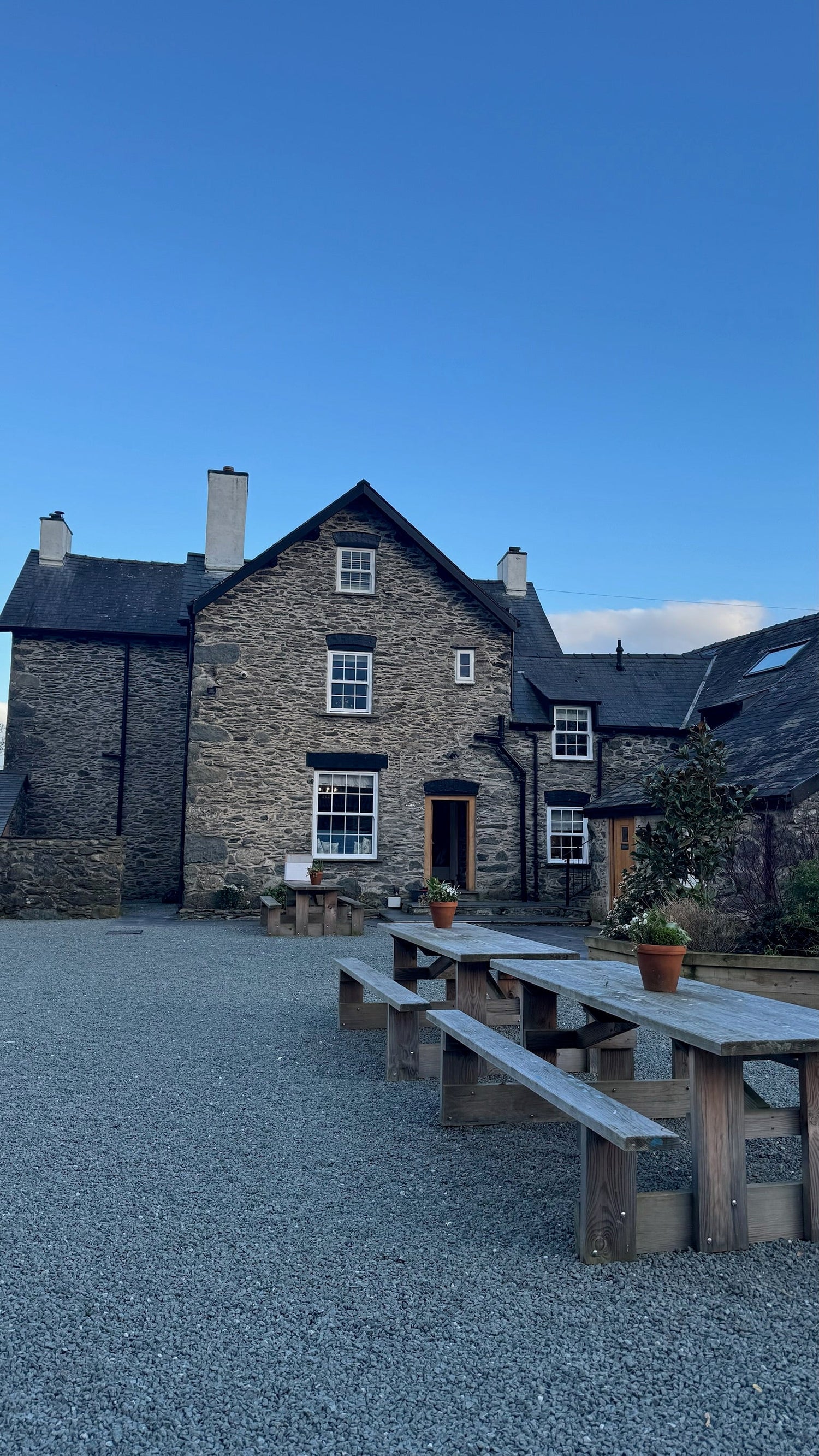 Rustic stone cottage with wooden picnic tables under a clear blue sky