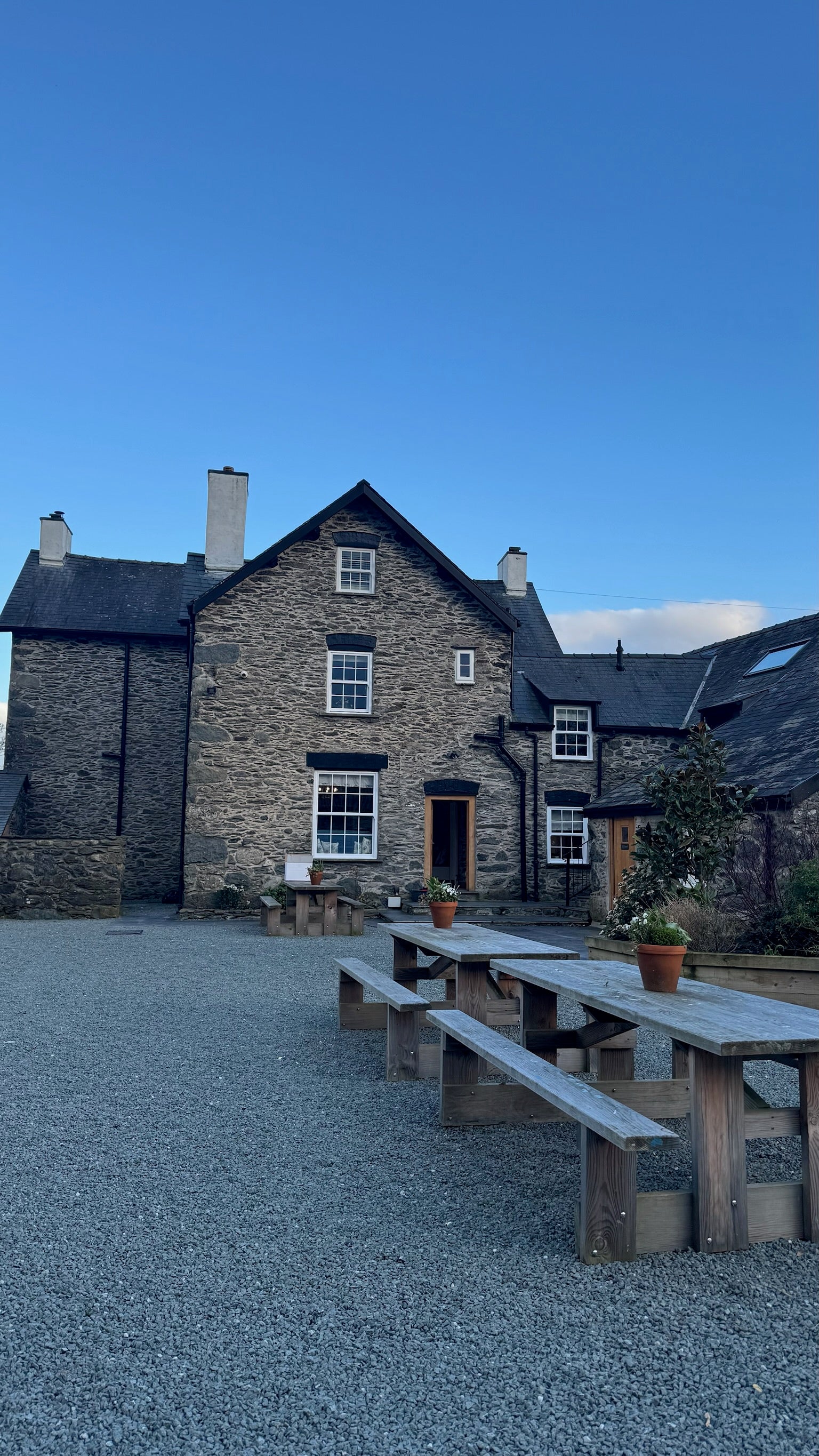 Rustic stone cottage with wooden picnic tables under a clear blue sky