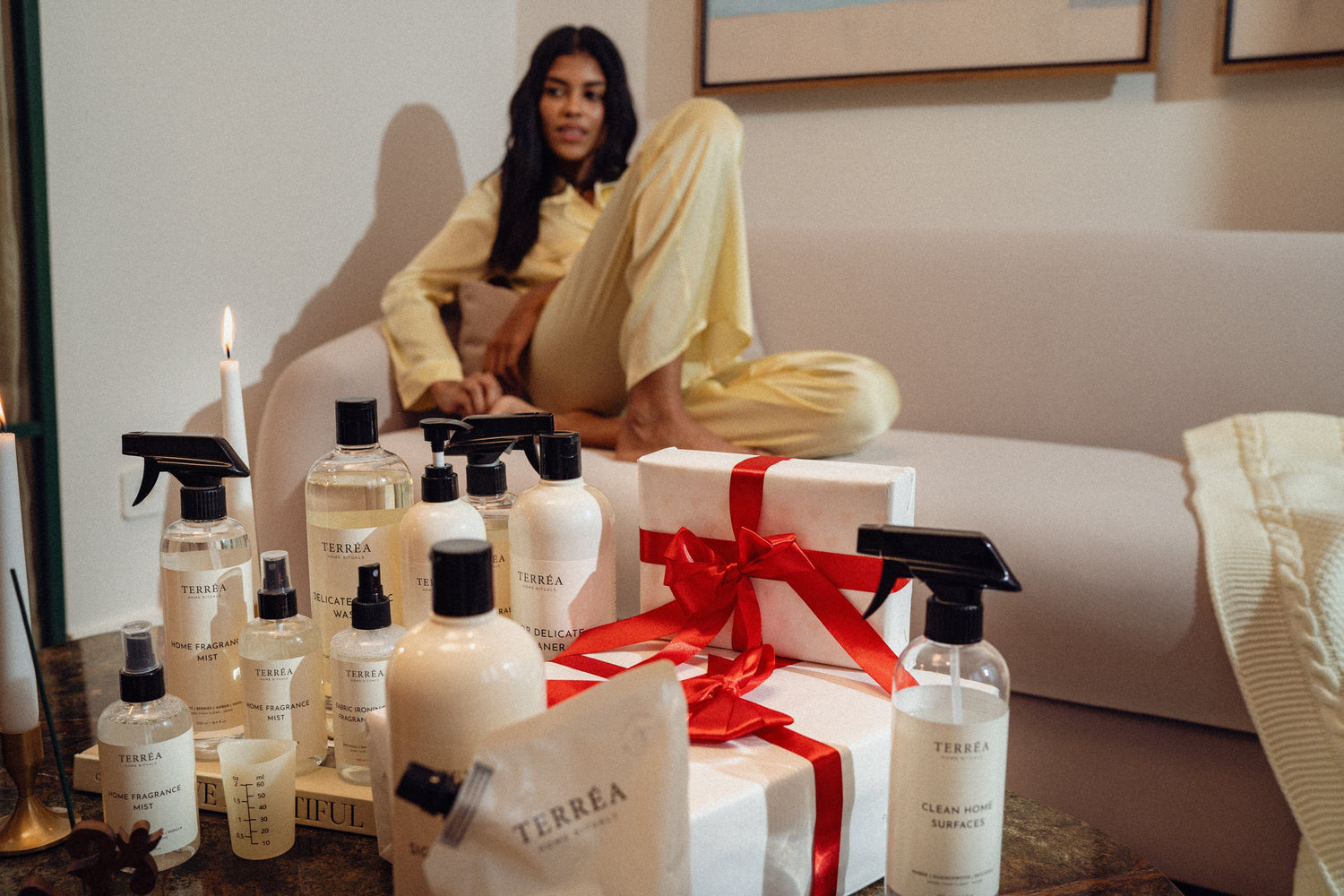 Terréa gift scene with wrapped presents and home care bottles, woman relaxing on a sofa