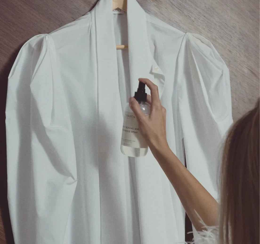 Hand spraying eco-friendly fabric freshener on white shirt, sustainable home care