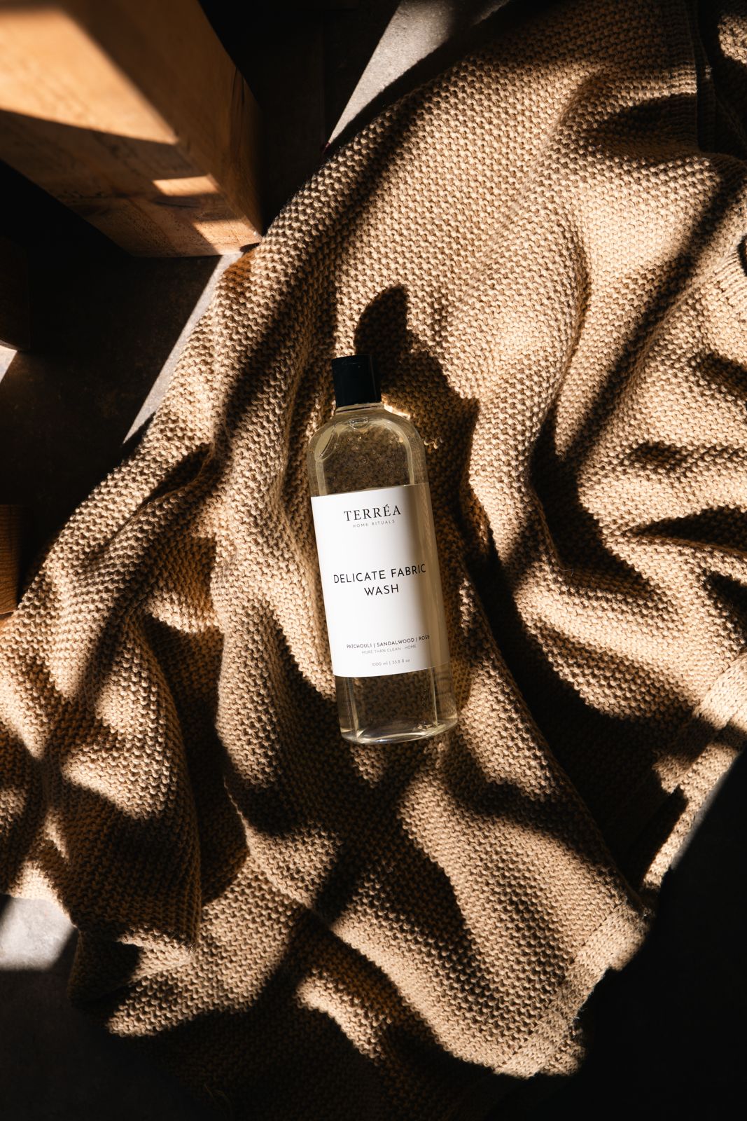 Delicate fabric wash bottle on textured knit blanket, natural light shadows, eco-conscious laundry care