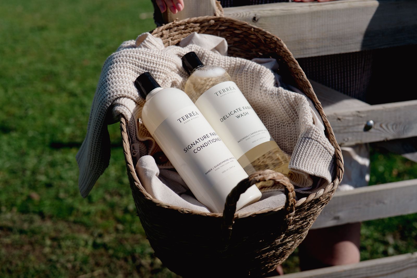 Terréa Delicate Fabric Wash 1000 ml and Signature Fabric Conditioner 1000 ml in a woven basket with knit throw by a fence.