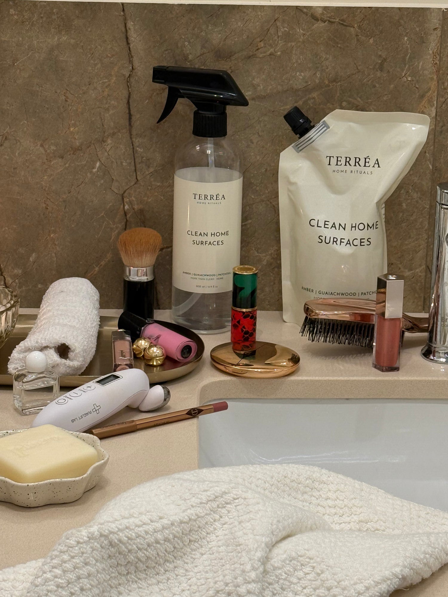 Terréa Clean Home Surfaces spray bottle and refill pouch on bathroom counter with toiletries and towel