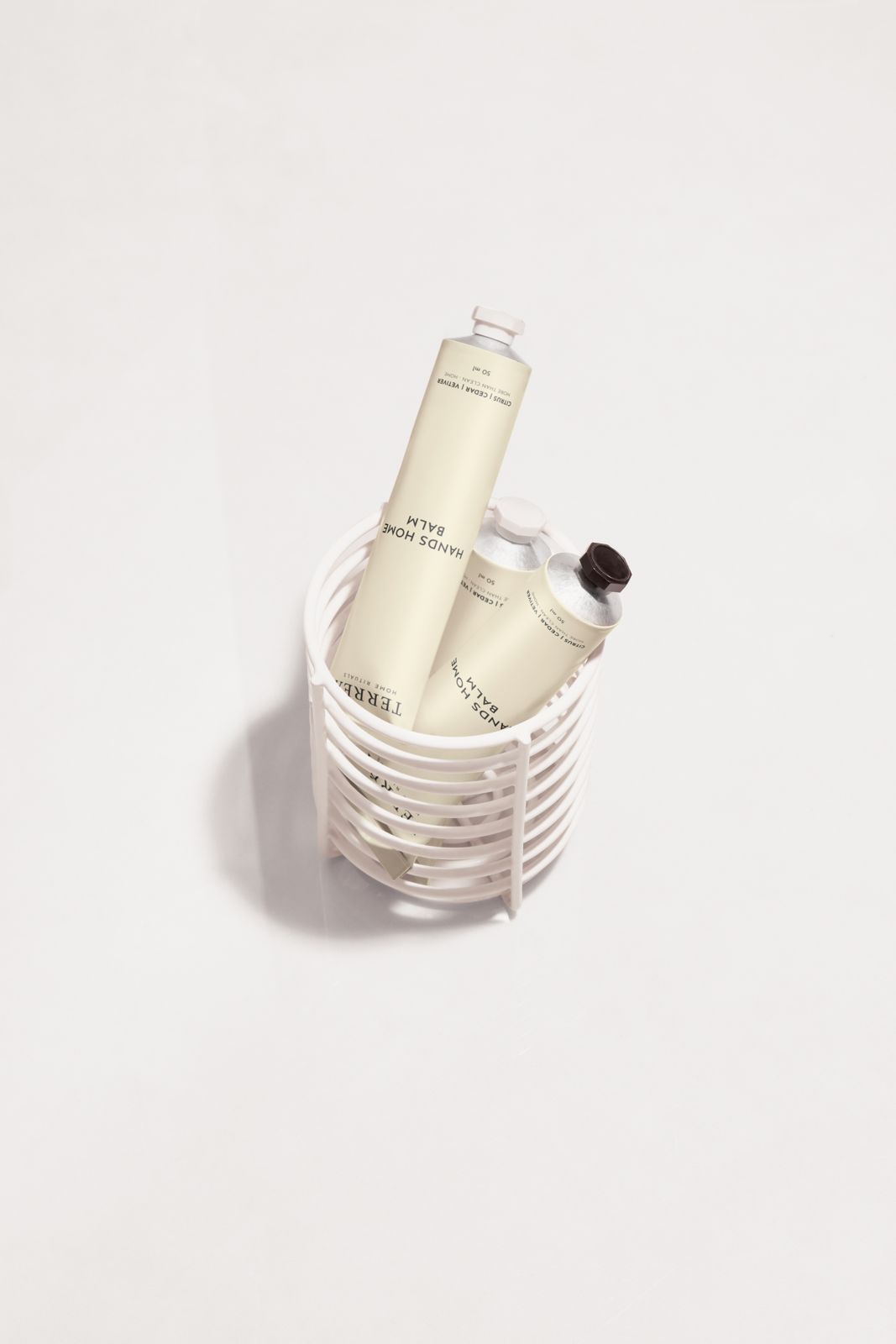 Terréa Hands Home Balm tubes placed inside a white ribbed basket on a clean white surface.
