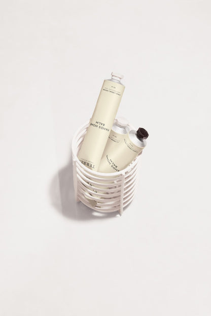 Terréa Hands Home Balm tubes placed inside a white ribbed basket on a clean white surface.