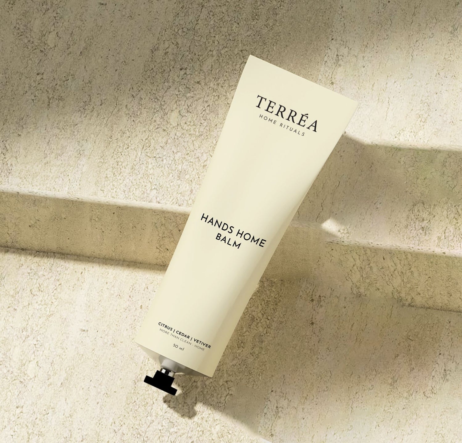 Terréa Hands Home Balm tube on a textured stone surface with soft natural shadows.