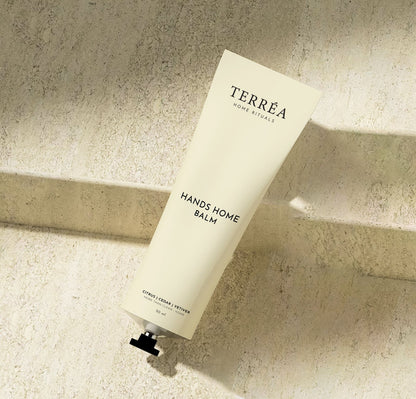 Terréa Hands Home Balm tube on a textured stone surface with soft natural shadows.
