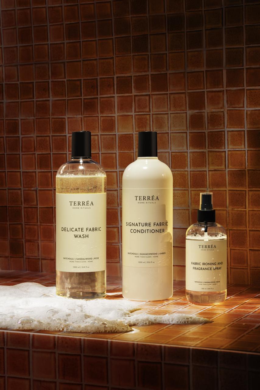 Three bottles of Terrea fabric care products on a tiled surface with a brown tile background.