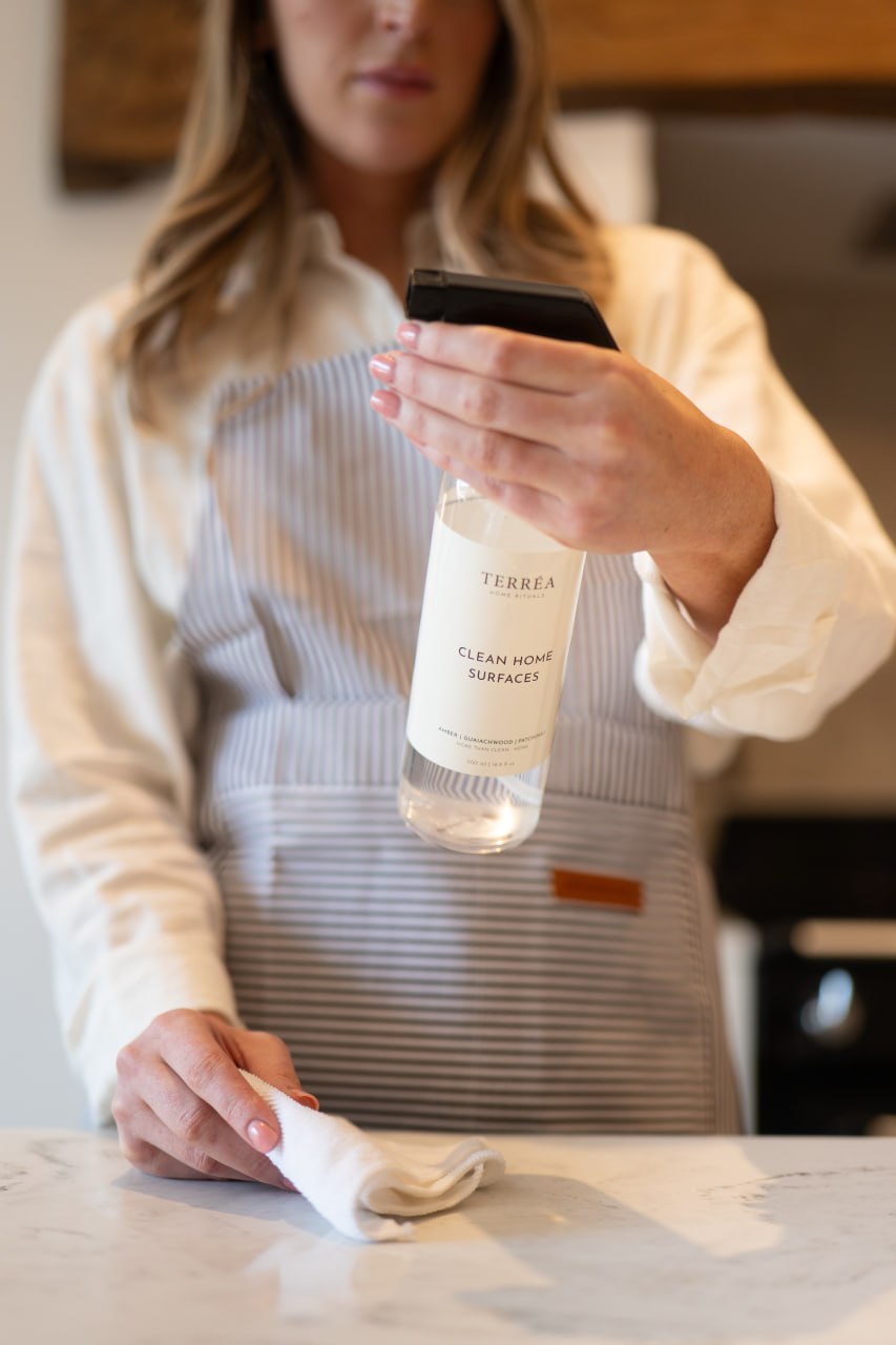 Terréa Clean Home Surfaces spray held over a marble worktop as a cloth wipes the surface.