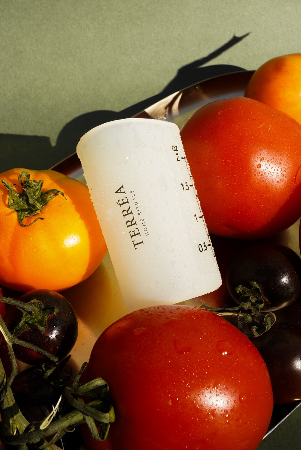 Terréa silicone measuring cup styled among ripe tomatoes and dark berries on a golden tray, with warm sunlight and crisp shadows.