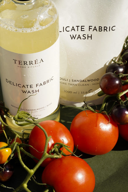 Terréa Delicate Fabric Wash bottle and refill pouch styled with ripe tomatoes and dark berries against an olive-green backdrop, with warm sunlight highlighting fresh droplets and glossy surfaces.