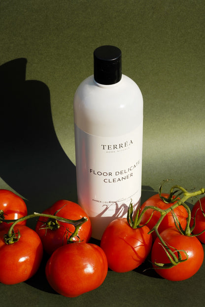 Terréa Floor Delicate Cleaner styled with ripe tomatoes against an olive-green backdrop, with warm directional sunlight and a strong sculptural shadow.