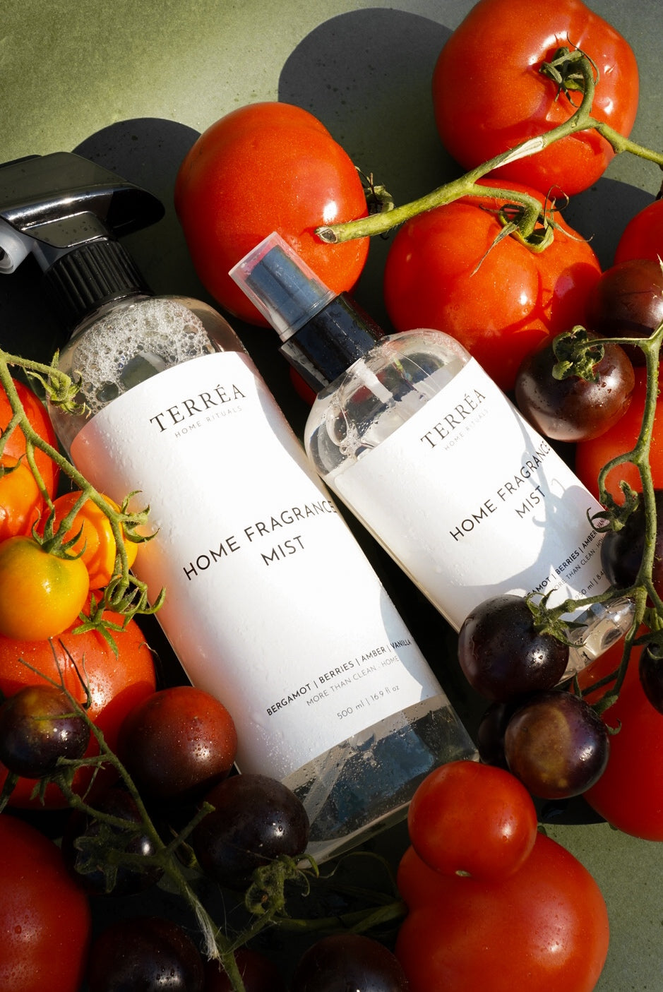 Two Terréa Home Fragrance Mist bottles nestled among ripe tomatoes and dark berries against an olive-green backdrop, with warm sunlight, fresh droplets and deep botanical shadows.
