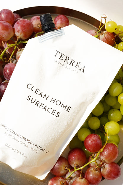 Terréa Clean Home Surfaces refill pouch styled on a golden tray with red and green grapes, with fresh droplets catching the warm sunlight.
