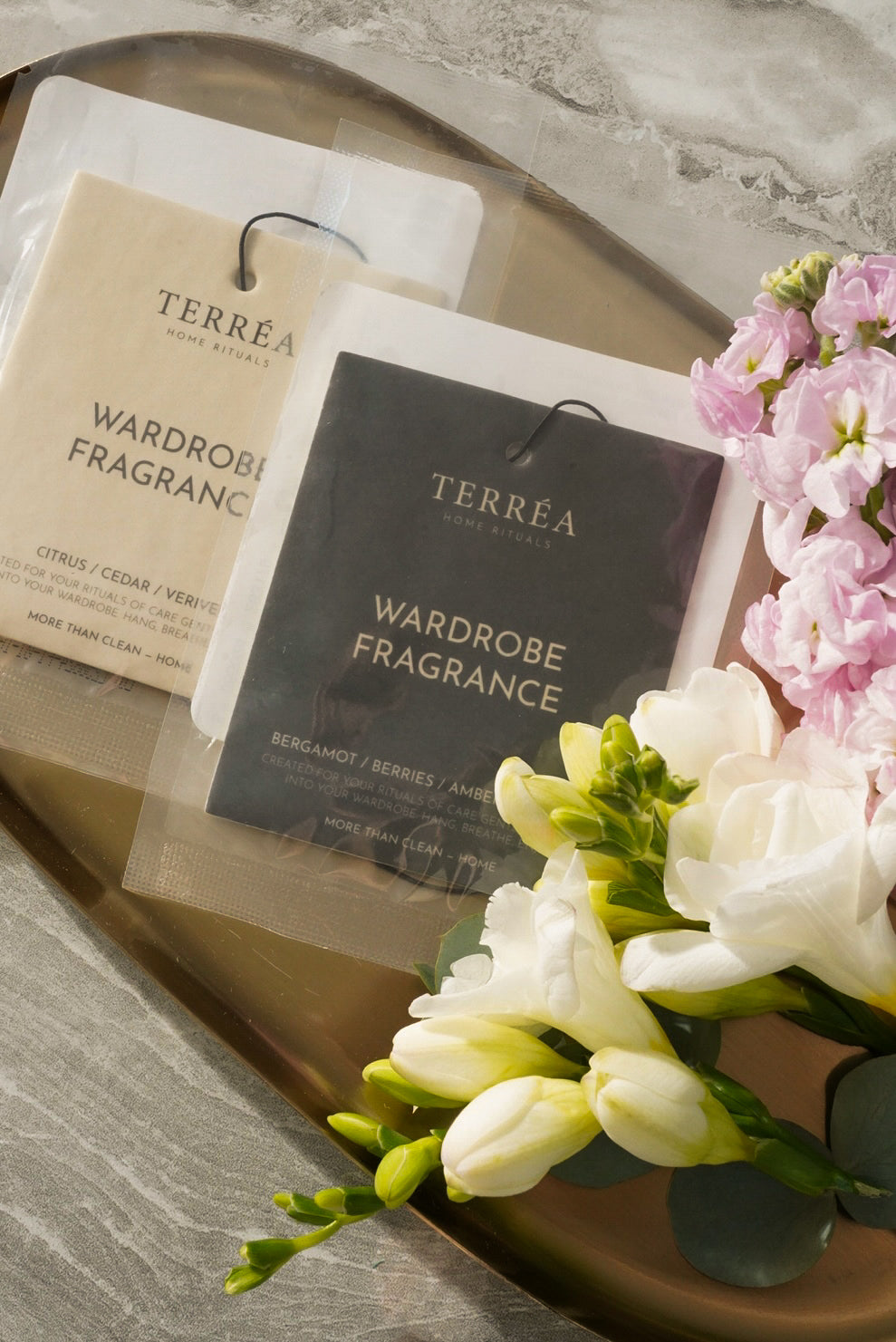 Terréa Wardrobe Fragrance sachets on a brass tray with pink stock flowers, white freesia and eucalyptus.