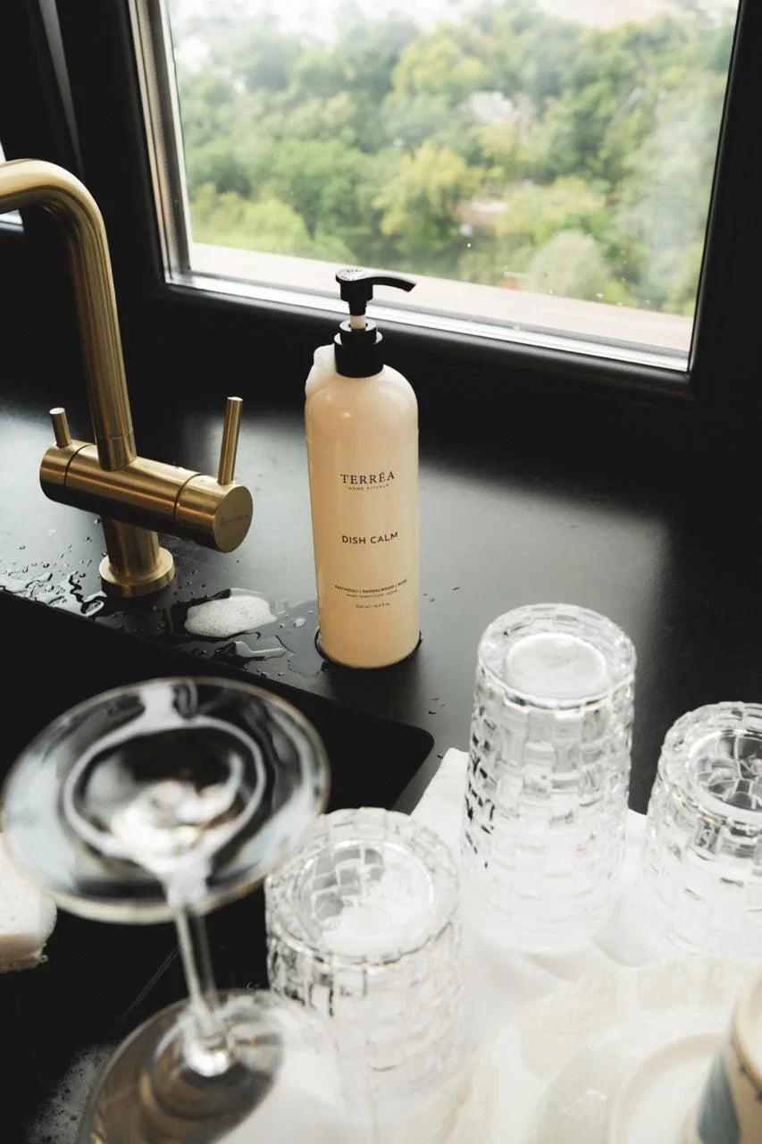 Bottle of Terrea Care on a dark surface with glasses and a gold faucet.