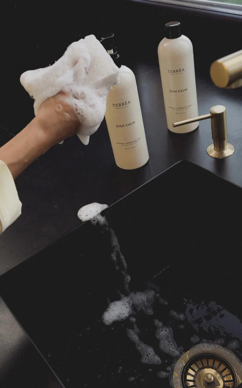 Person cleaning a sink with soapy hands, bottles in the background