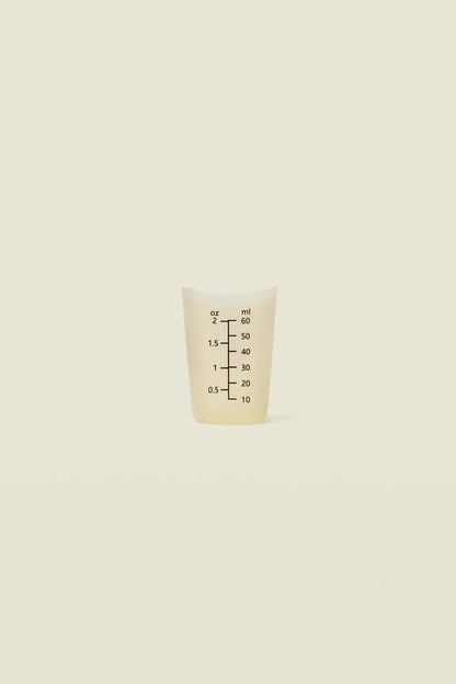 Small white measuring cup with black markings on a beige background