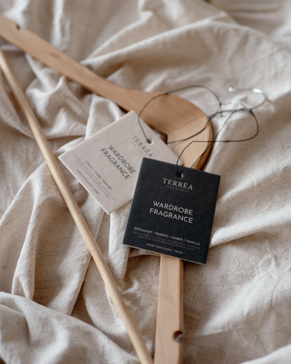 Terréa Wardrobe Fragrance tags resting on soft linen with wooden hangers, creating a quiet wardrobe-care ritual.