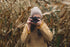 Terréa autumn photographer lifting a camera amid golden leaves; a quiet, mindful moment.”