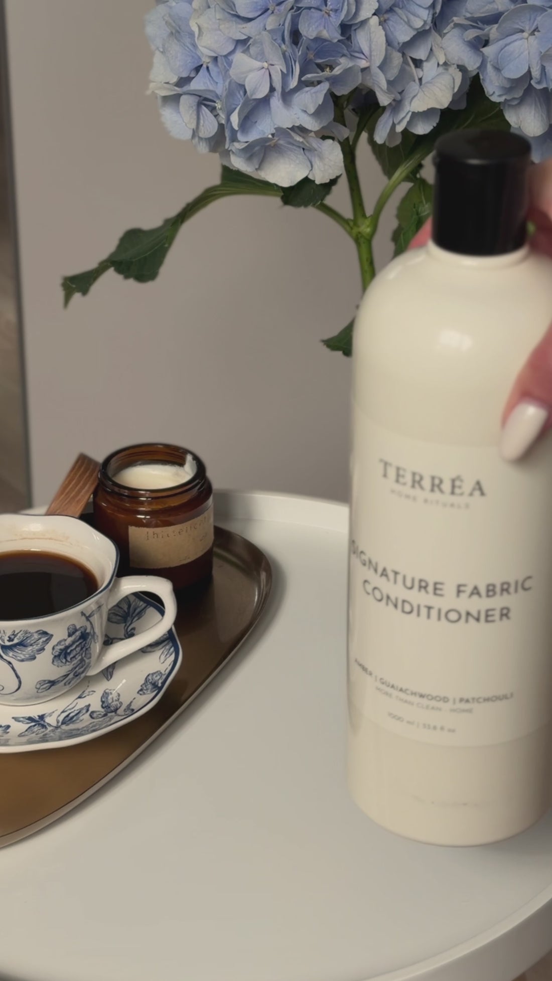 A close-up video still of Terréa Signature Fabric Conditioner beside its refill pouch, with blue hydrangeas and a quiet tea tray in the background.