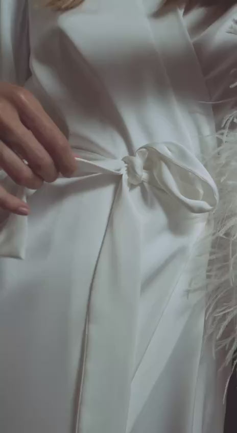 woman in a feather-trim robe spritzes a white blouse with Ironing Water; light, crease-easing fabric ritual.