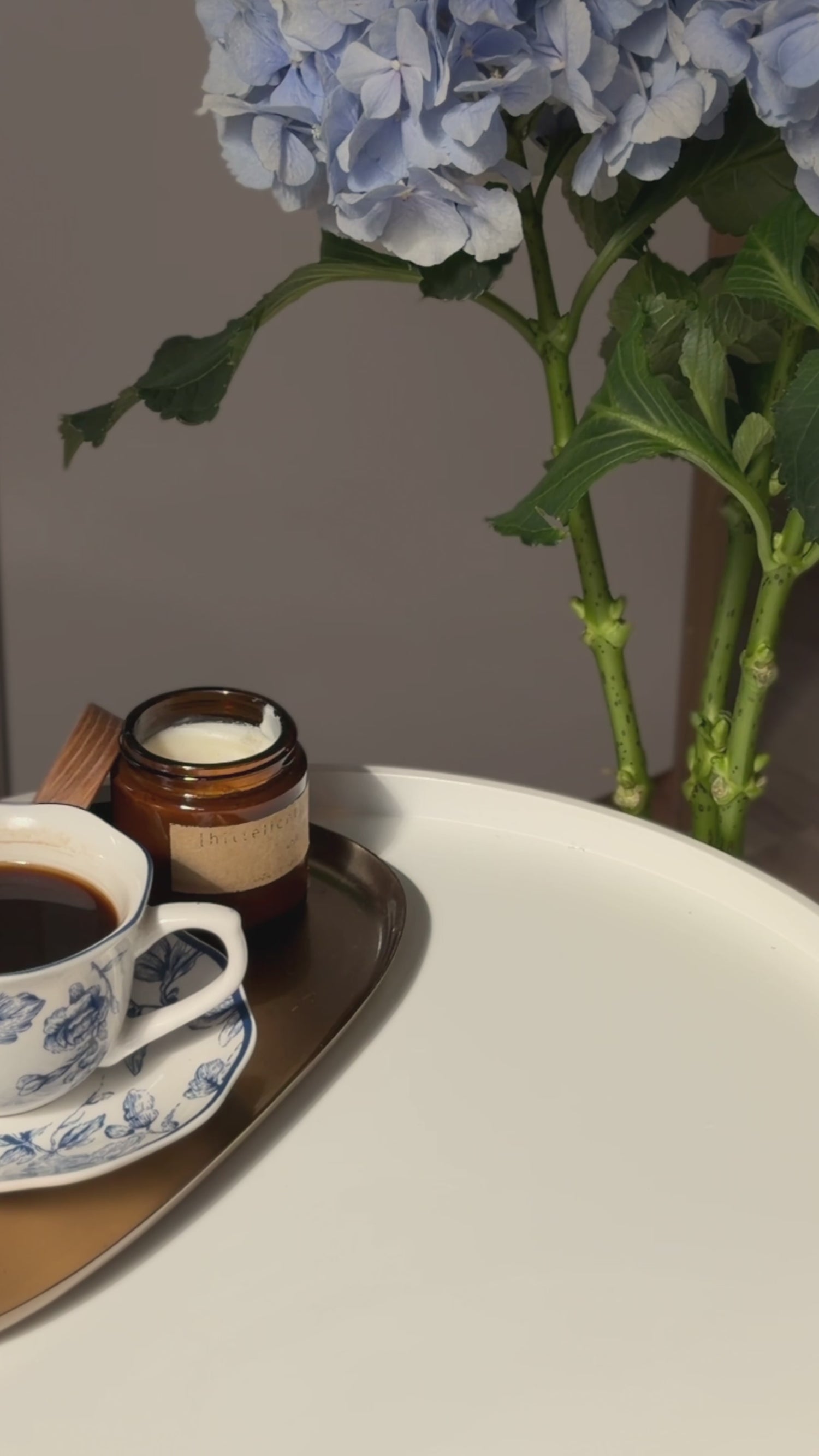 A close-up video still of Terréa Floor Delicate Cleaner beside its refill pouch, styled with blue hydrangeas and a quiet cup of tea.