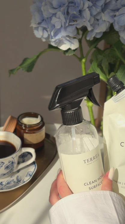 A close-up video still of Terréa Clean Home Surfaces being held beside a refill pouch, blue hydrangeas and a quiet tea tray.