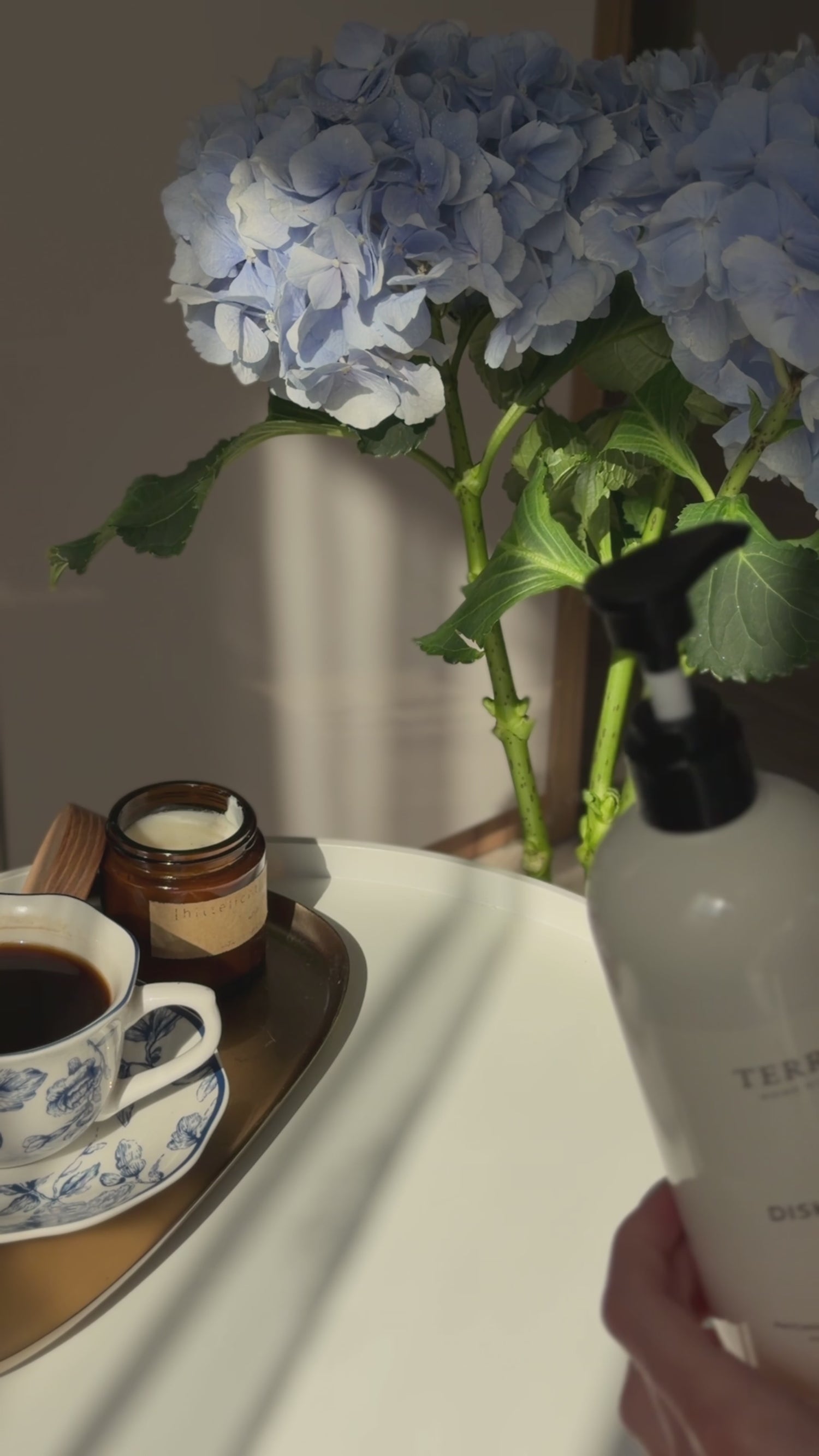 A close-up video still of Terréa Dish Calm being refilled from its soft refill pouch, styled with blue hydrangeas and a quiet tea moment.