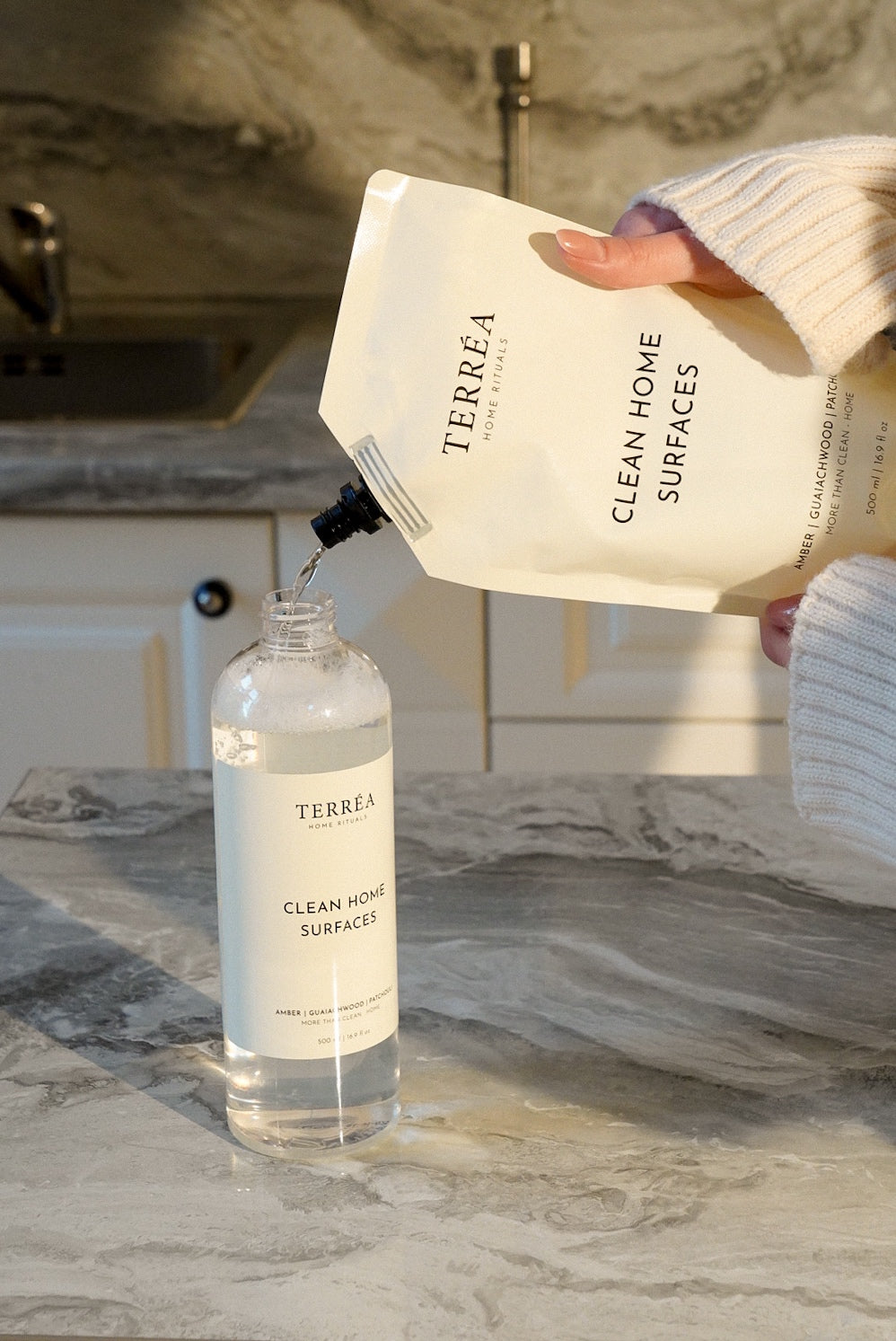Refilling a Clean Home Surfaces spray bottle from the Terréa refill pouch on a marble worktop